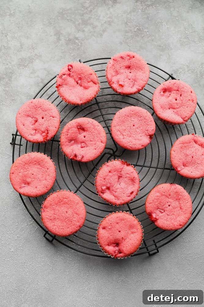 A row of unfrosted, cooked vegan strawberry cupcakes with a lovely pinkish-red hue, cooling on a wire rack.