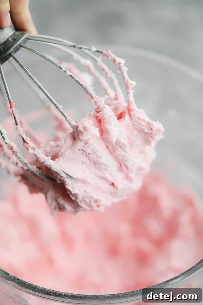 Close-up of creamy, pink strawberry buttercream frosting clinging to a whisk in a mixing bowl.