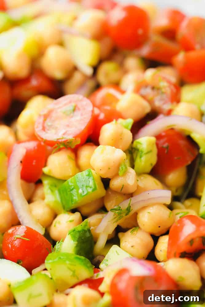 Close up of a fresh chickpea salad with vibrant tomatoes, crisp cucumbers, and leafy greens, ready for a healthy meal.