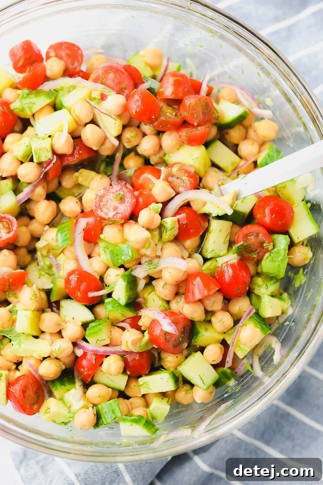 A large glass bowl filled with a vibrant chickpea and tomato salad, showcasing its fresh ingredients and inviting colors.