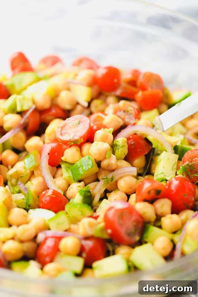 Close up shot of a vibrant chickpea salad in a clear glass bowl, featuring diced tomatoes, cucumbers, and red onion, highlighting its fresh ingredients.