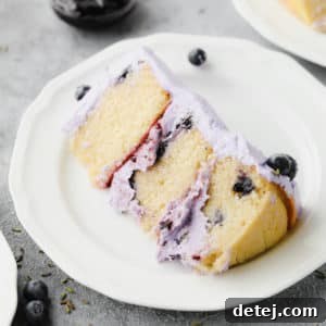 A beautiful slice of vegan lemon blueberry lavender cake on a white plate, garnished with fresh blueberries and topped with smooth purple frosting.