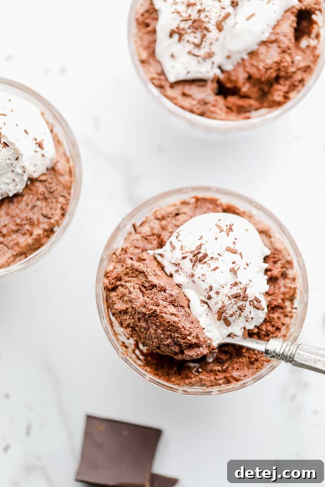 Overhead view of a spoon scooping a generous bite of airy vegan chocolate mousse from a glass cup, highlighting its light texture.