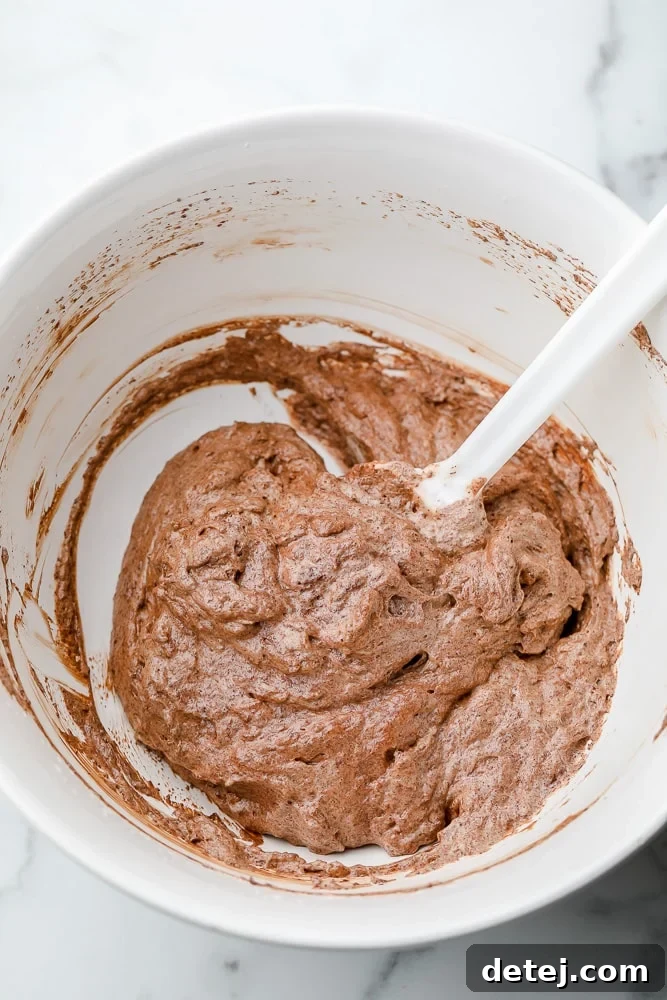 White spatula mixing a light chocolate mousse in a white bowl, showing its creamy and airy texture.