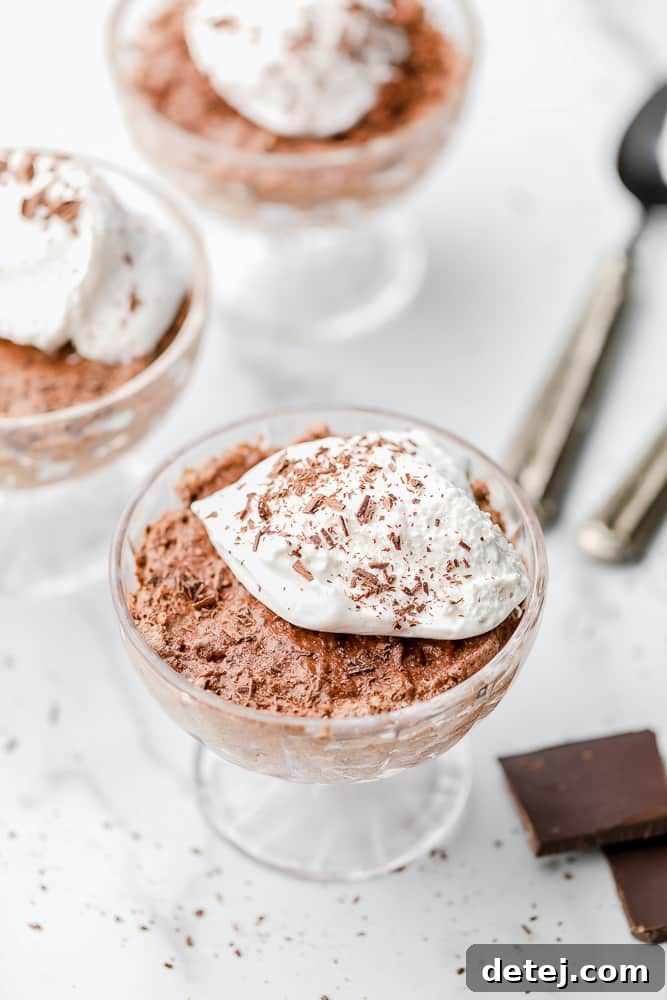 Three glass dessert cups filled with vegan chocolate mousse, garnished with vegan whipped cream and chocolate shavings.