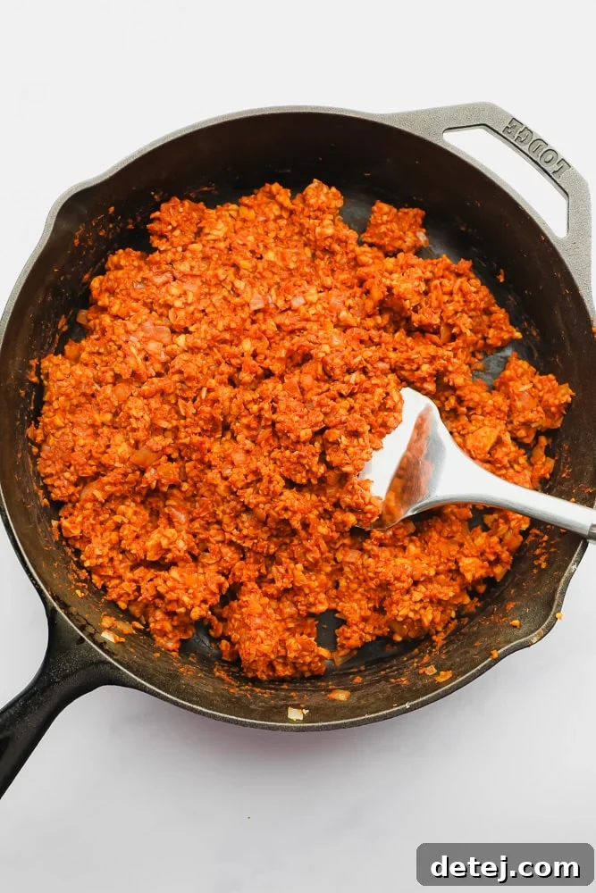 Close-up of vibrant orange tempeh taco meat sizzling in a cast iron skillet, perfectly seasoned and ready for tacos.