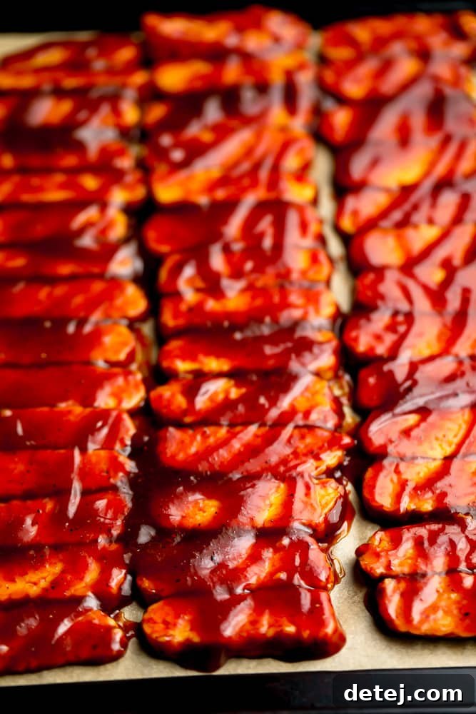 Uncooked vegan tempeh ribs smothered in BBQ sauce on parchment paper