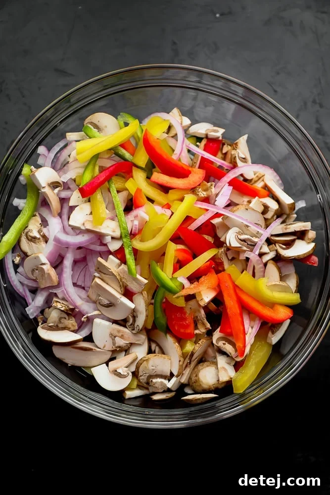 Large glass bowls filled with precisely sliced bell peppers, red onion, and mushrooms, meticulously prepped for cooking vegetarian fajitas.