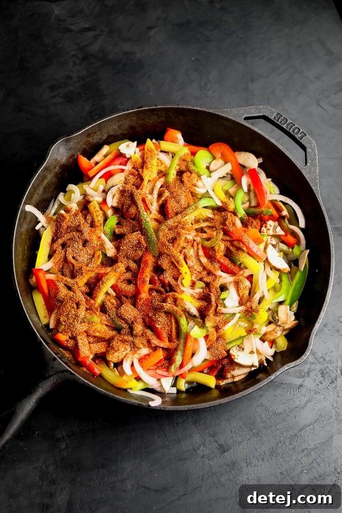 Raw sliced bell peppers, onions, and mushrooms with a generous sprinkle of fajita seasonings, all ready in a black skillet before cooking.