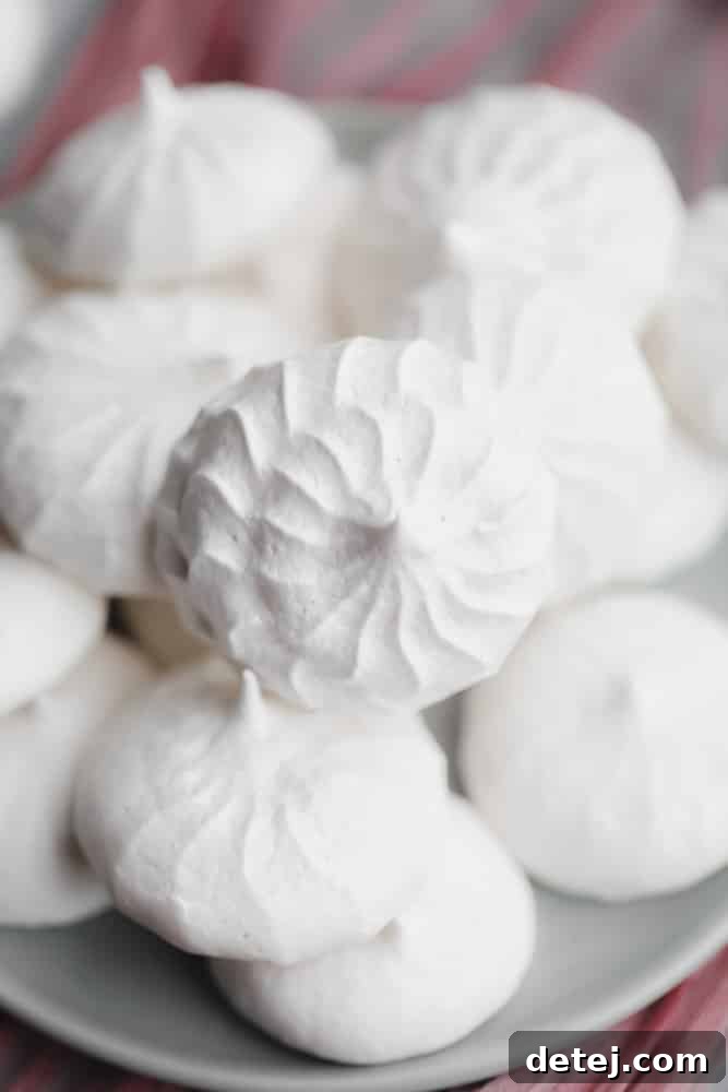 Close up on a pile of white vegan meringues cookies on a small grey plate, showing their delicate texture.