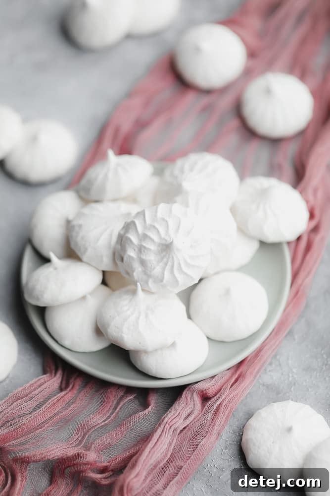 White vegan meringues cookies meticulously arranged on a small grey plate.