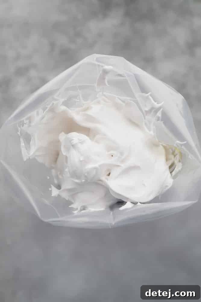 Overhead view of a white creamy batter being carefully spooned into a piping bag.