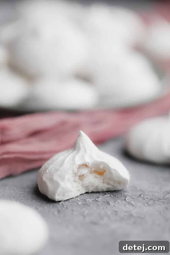A close-up of a white meringue cookie with a bite taken out, revealing its airy interior.