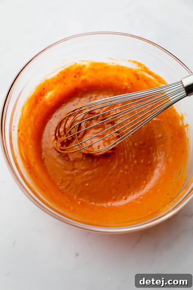 a metal whisk in a glass bowl with orange sauce