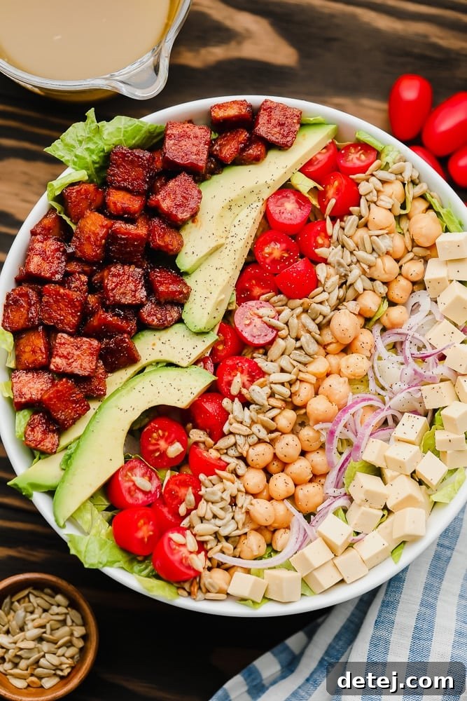 lines of vegan bacon, avocado, tomatoes, seeds, and beans on top of lettuce in a white bowl