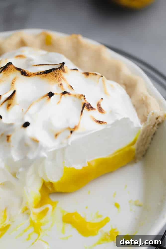 Fluffy Vegan Lemon Meringue Bliss 2 Close-up on a slice of Vegan Lemon Meringue Pie, revealing layers of golden crust, creamy lemon curd, and fluffy toasted meringue.