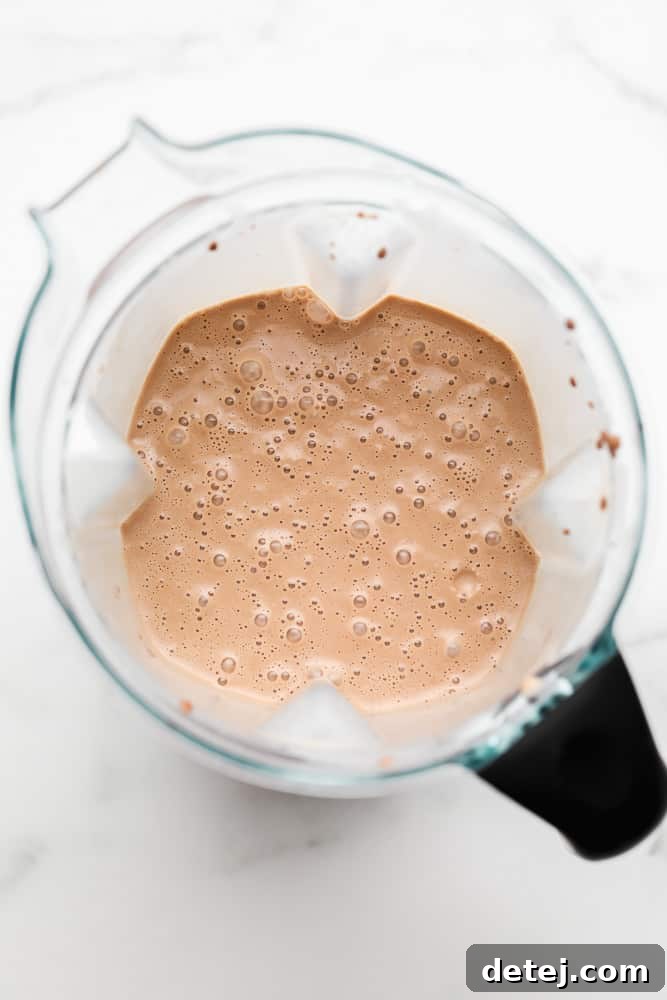 Plant-Based Power Shake 4 A close-up shot of the bubbly, rich chocolate liquid swirling in a blender, showcasing the smooth texture of the vegan protein shake as it's being prepared.