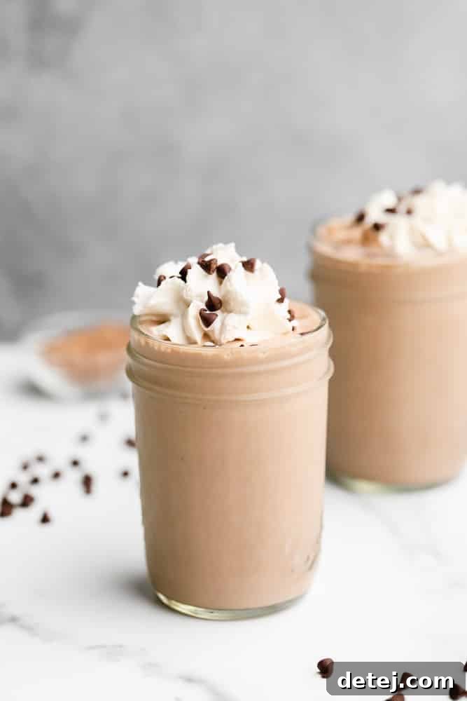 Plant-Based Power Shake 5 A mason jar filled with a thick, chocolate vegan protein shake, topped generously with creamy vegan whipped cream and sprinkled with mini chocolate chips, ready to be enjoyed.