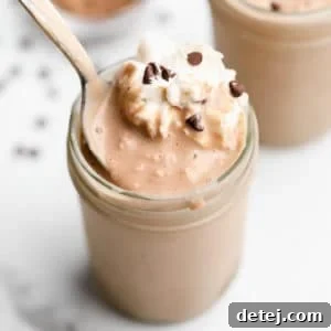 A spoon scooping a rich chocolate vegan protein shake from a mason jar