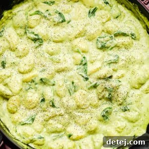 close up of large pot filled with a green cream sauce and gnocchi
