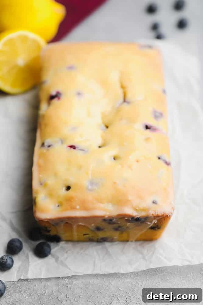 glazed loaf of blueberry and lemon bread on a piece of parchment paper, ready to be sliced