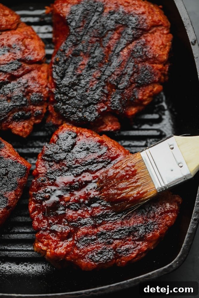 Brushing a vibrant red marinade onto a sizzling, charred vegan steak in a cast iron grill pan, ready for summer barbecue enjoyment.