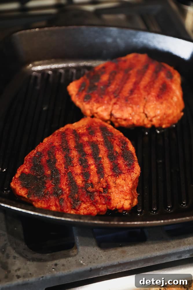 Two orange seitan patties searing beautifully in a black cast iron grill pan, developing a rich, charred crust.