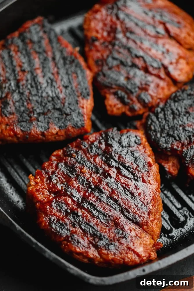 Four beautifully charred vegan steaks, sizzling in a black grill pan, ready to be served or sliced.