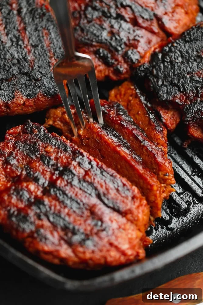 A fork lifting a delicious slice of vegan steak from a black grill pan, highlighting its tender, juicy texture.