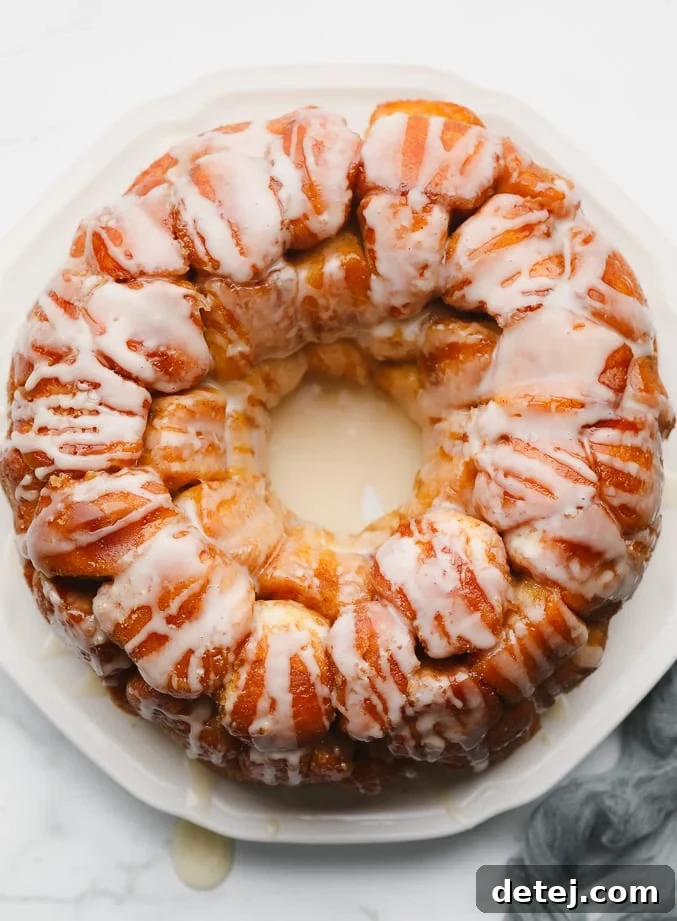 Baked golden brown monkey bread on a white plate, covered in white icing, ready to be pulled apart and enjoyed.