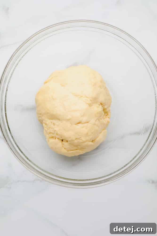 Small ball of raw, freshly mixed bread dough in a clear glass bowl, showcasing its soft consistency.