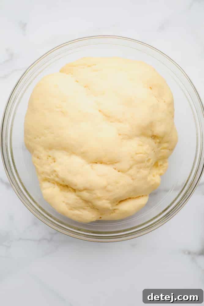 Large ball of raw bread dough in a glass bowl, significantly risen and ready for shaping.