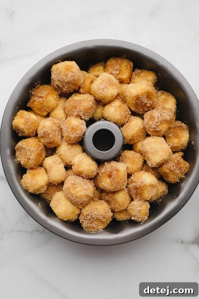 Close-up of small balls of cinnamon sugar-coated dough layered neatly in a bundt pan, ready for baking.