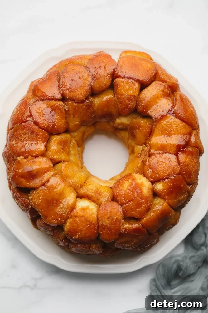 Baked golden brown monkey bread arranged in a perfect circle on a white plate, ready for glazing.