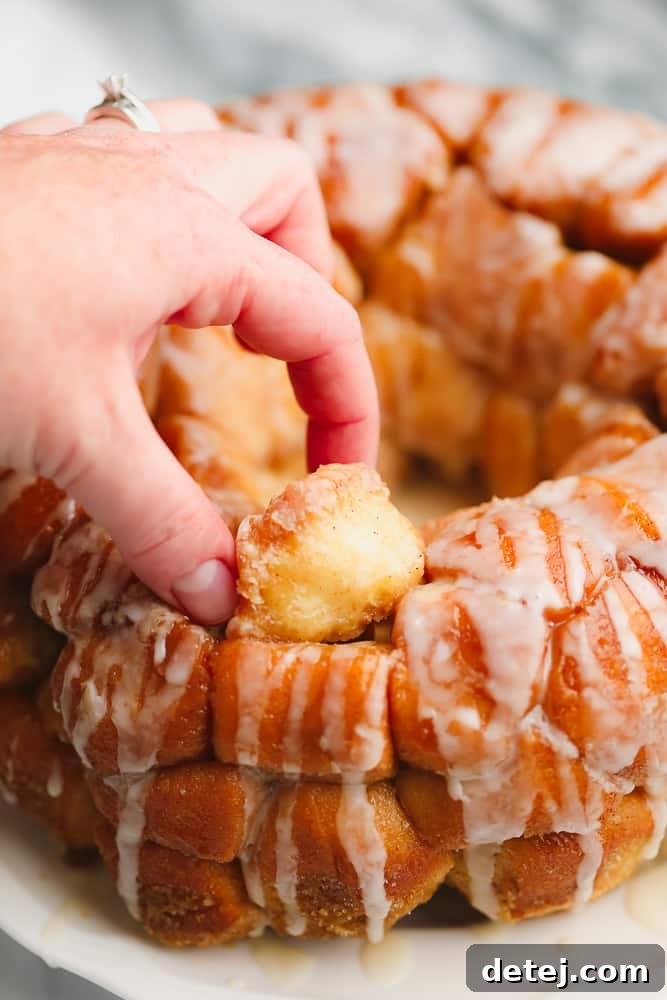 Woman's hand gently pulling a soft, golden brown ball of dough from a freshly baked loaf of vegan monkey bread.
