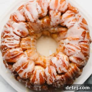 Baked golden brown monkey bread on a white plate, covered in white icing