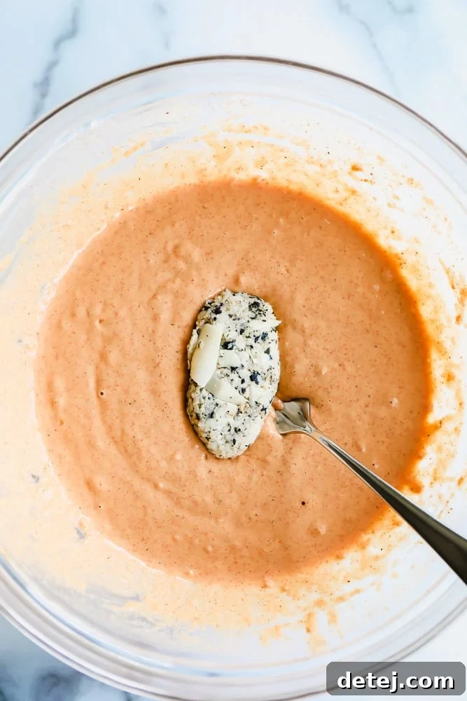 dipping a white vegan fish filet in an orange batter in a glass bowl