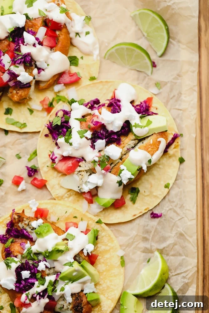 Overhead view of several vegan fish tacos on corn tortillas, topped with purple cabbage and white sauce, arranged neatly on parchment paper.