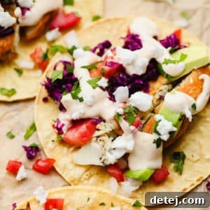 Close-up of a perfectly assembled vegan fish taco on a corn tortilla, adorned with purple cabbage and a luscious white sauce, resting on parchment paper.