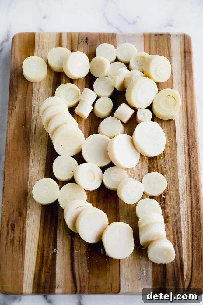 Close-up of neatly sliced white rounds of hearts of palm arranged on a wooden cutting board, ready for cooking.