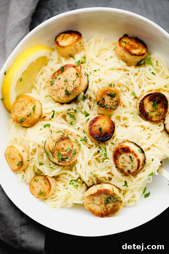 Cooked angel hair pasta topped generously with golden-brown vegan scallops and lemon-garlic sauce in a white bowl, garnished with fresh herbs.