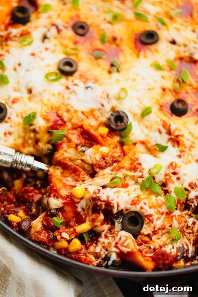 A serving spoon lifting a portion of cheesy vegan skillet enchiladas from the pan, highlighting the rich filling and melted cheese.