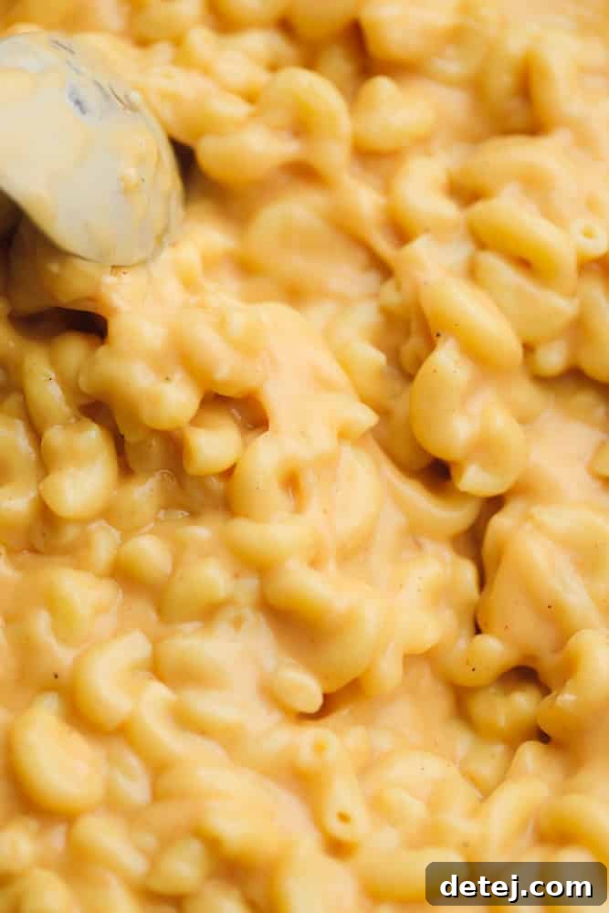 Close up of a metal spoon scooping saucy mac and cheese from a pot, highlighting its creamy texture.