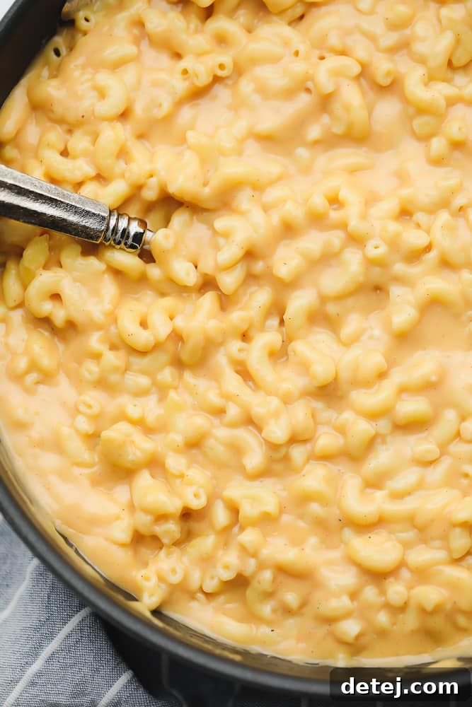 Close up on a metal spoon in a pot of saucy mac and cheese, ready to be served.