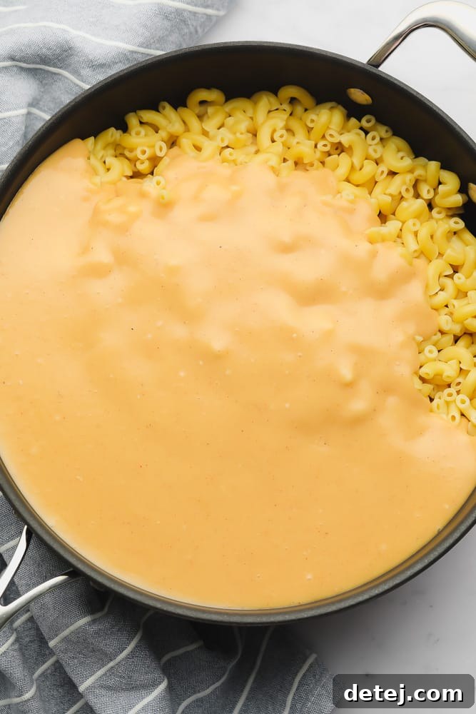 Orange cheese sauce covering cooked macaroni in a large black skillet, ready to be stirred.
