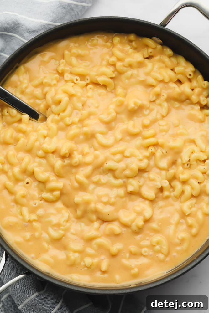 Vibrant orange mac and cheese in a large black skillet, glistening with creamy sauce.