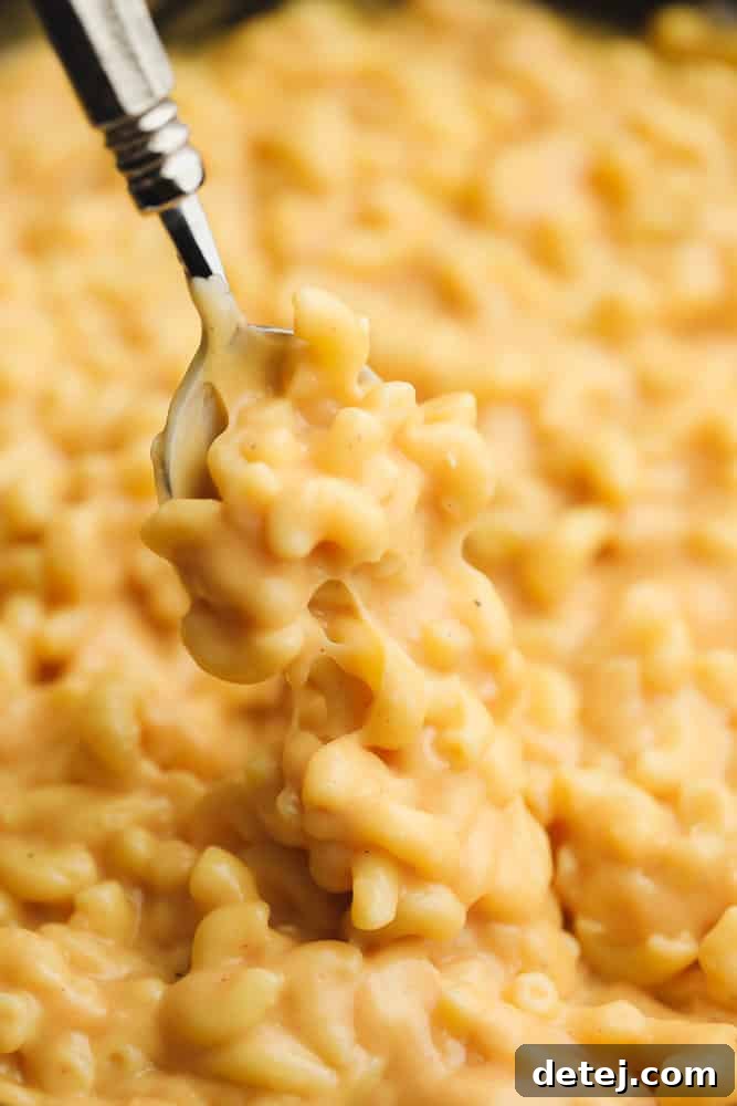 Close up of a spoon taking a generous scoop of dairy-free mac and cheese from a skillet, showcasing its texture.