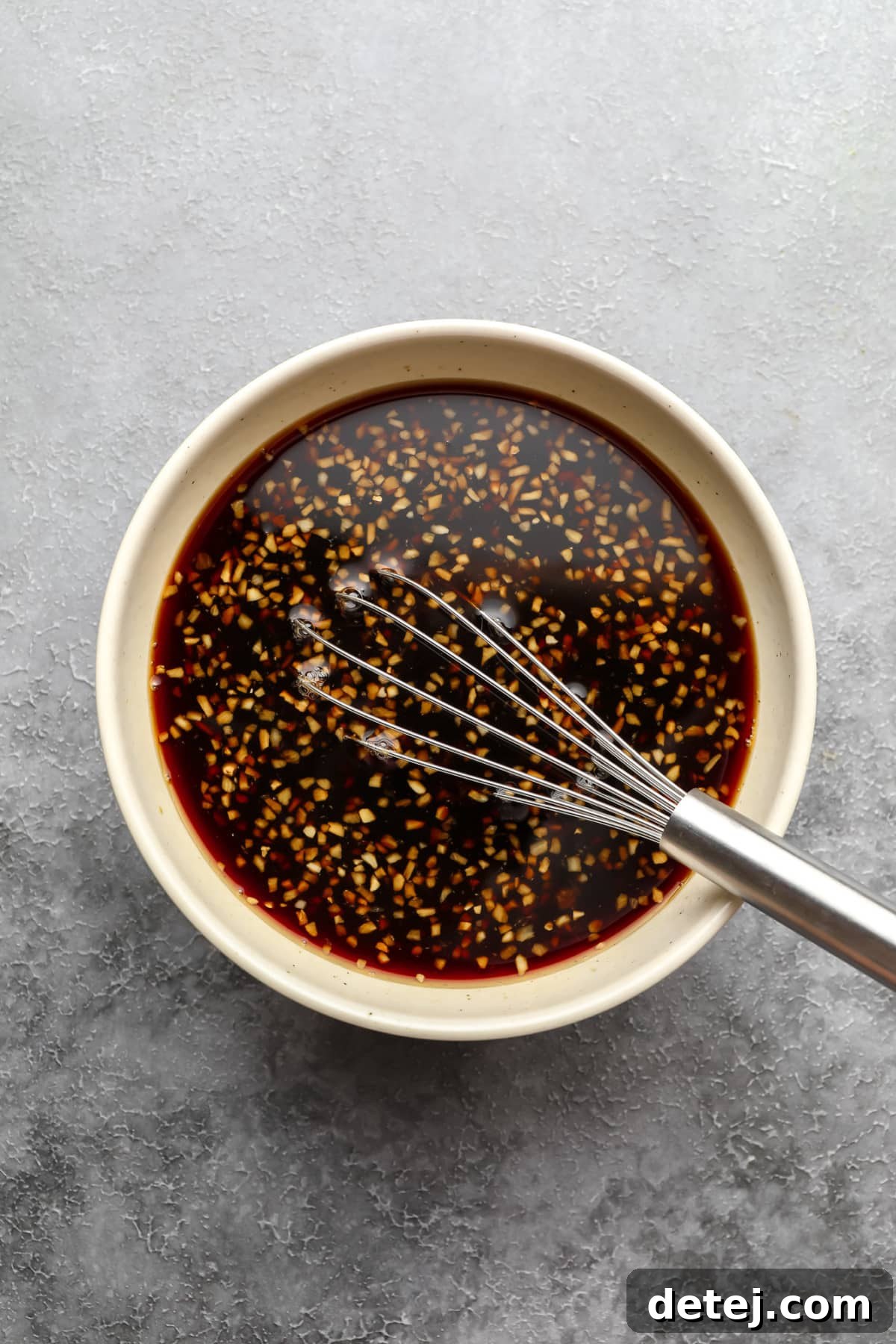 A small white bowl holds a rich, brown teriyaki sauce, placed on a grey background, ready to be incorporated into the dish.