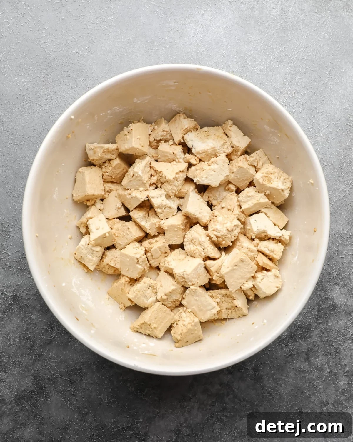 A bowl filled with bite-sized chunks of raw, pressed tofu, lightly coated and ready for cooking.