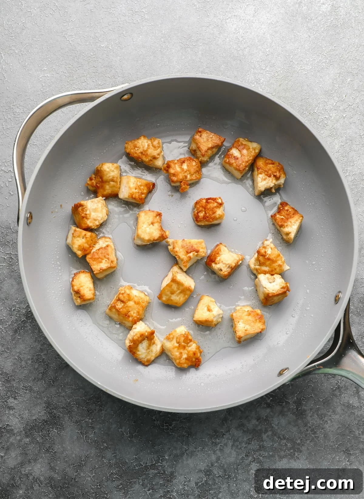 Crispy, golden-brown fried tofu pieces cooking in a grey non-stick pan, showing perfect texture development.